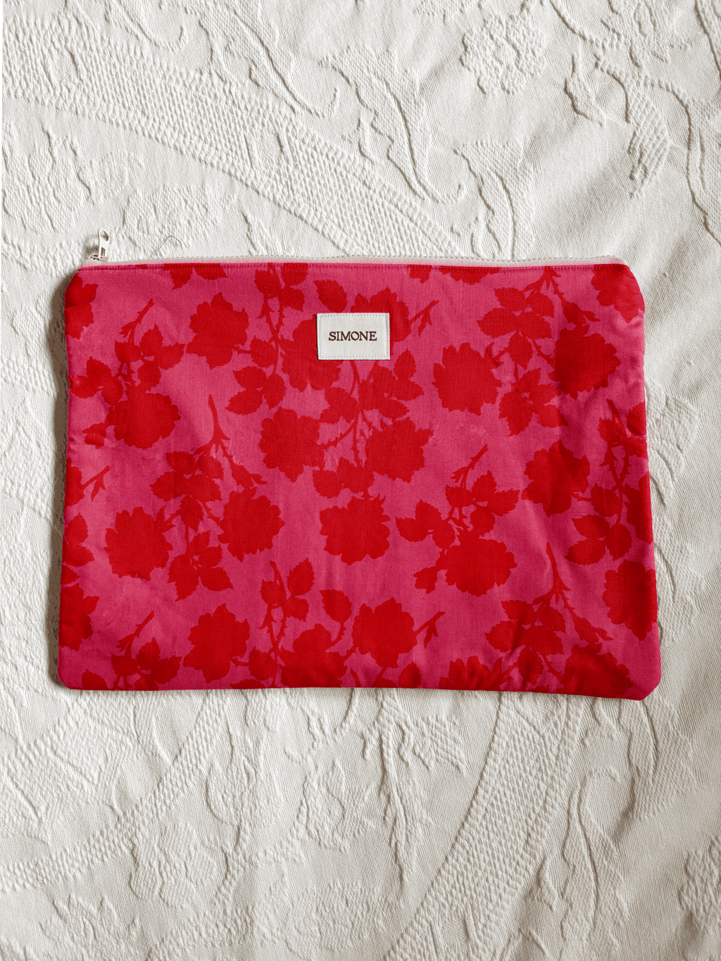 A zippered laptop sleeve with a bright pink floral exterior set against a textured off-white fabric background.