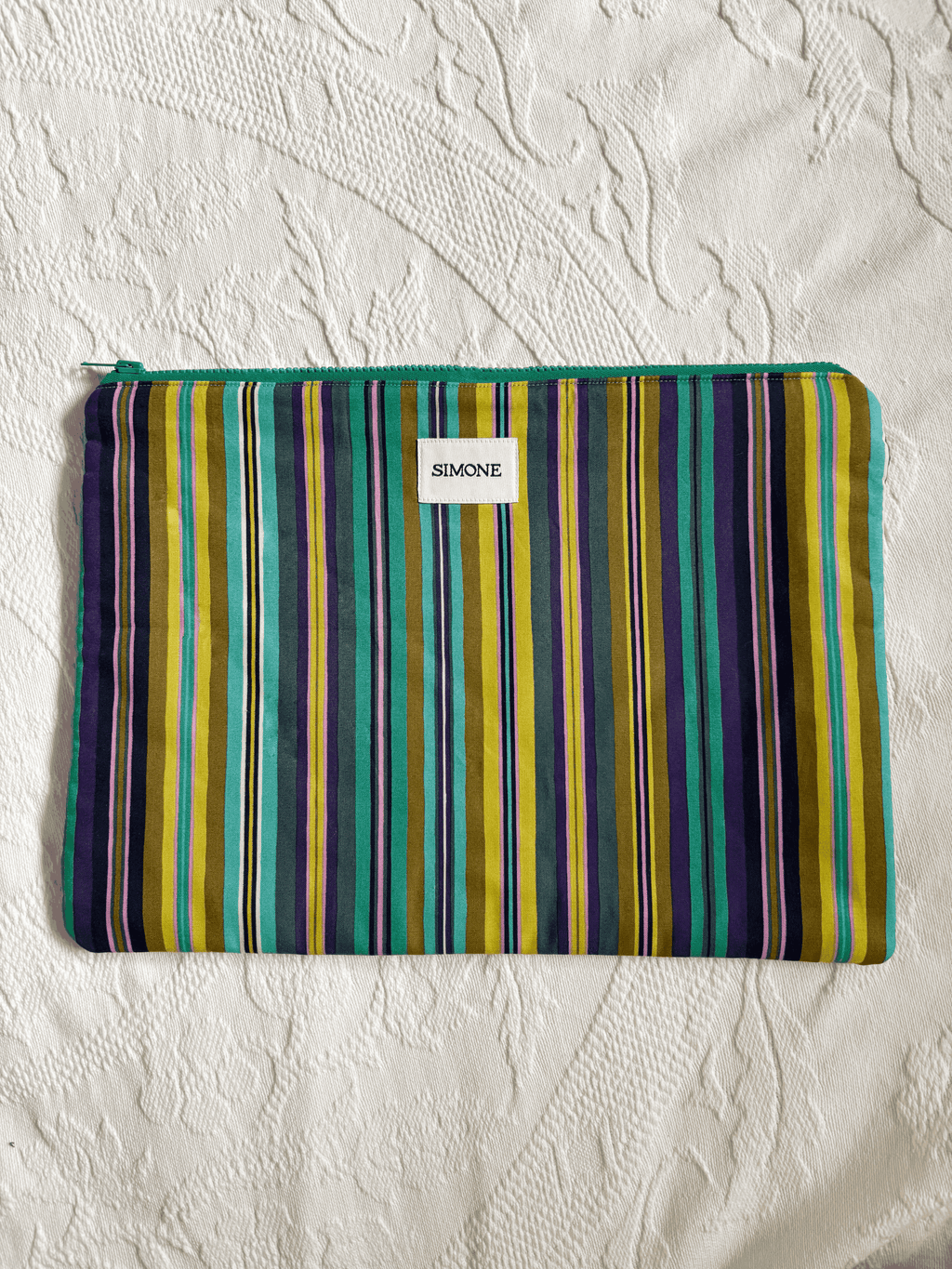 A zippered blue/green striped laptop sleeve with a small white label reading SIMONE