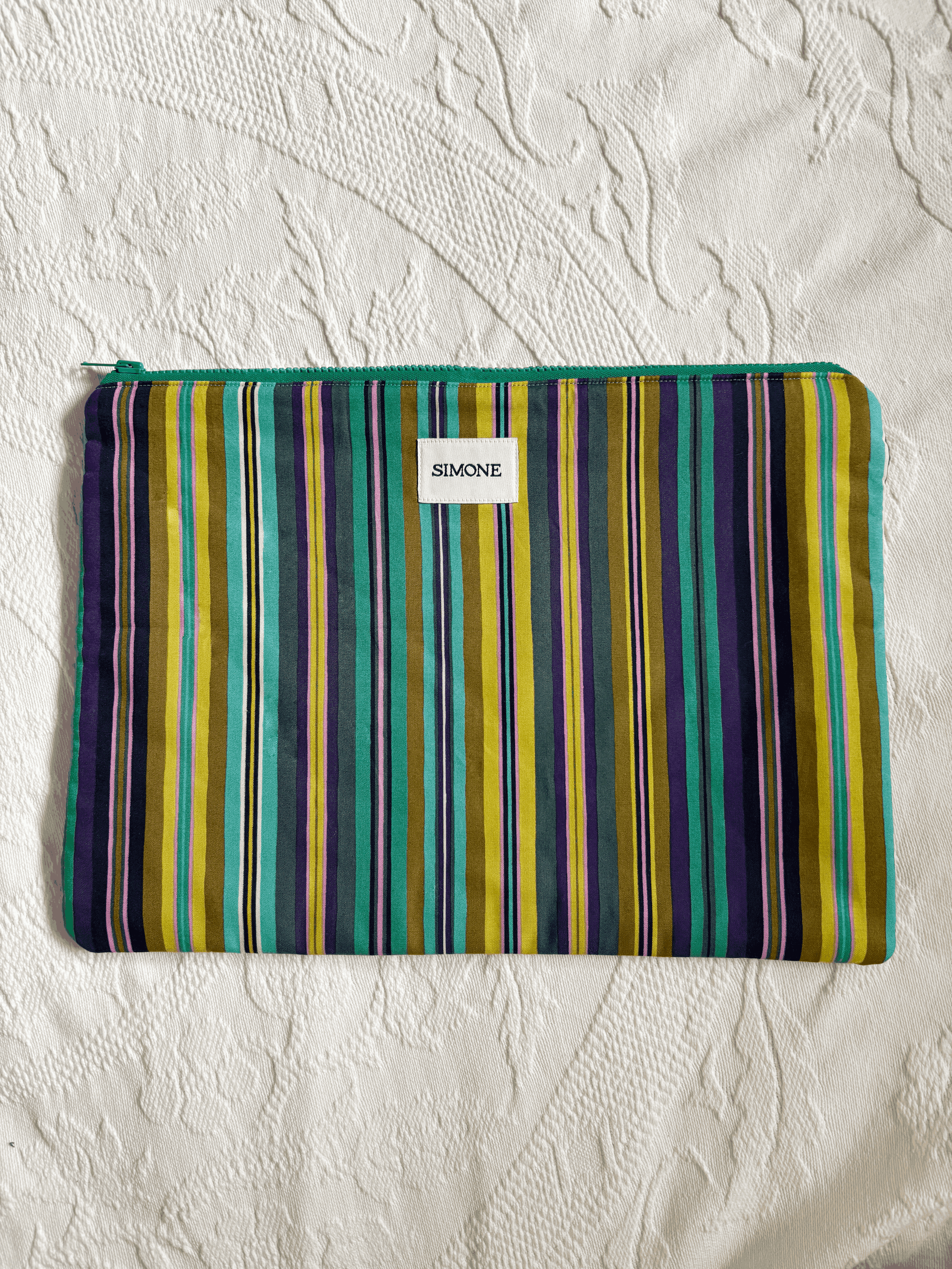A zippered blue/green striped laptop sleeve with a small white label reading SIMONE