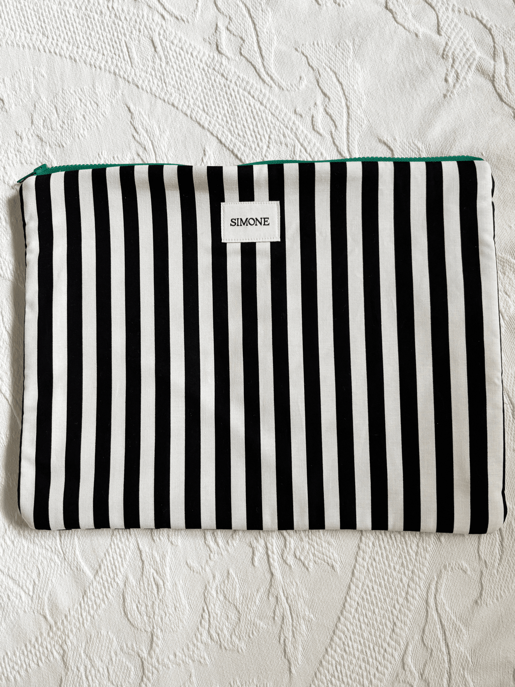 A black and white vertically striped zippered laptop sleeve sleeve with a small white label reading SIMONE, laid flat on a textured white surface.