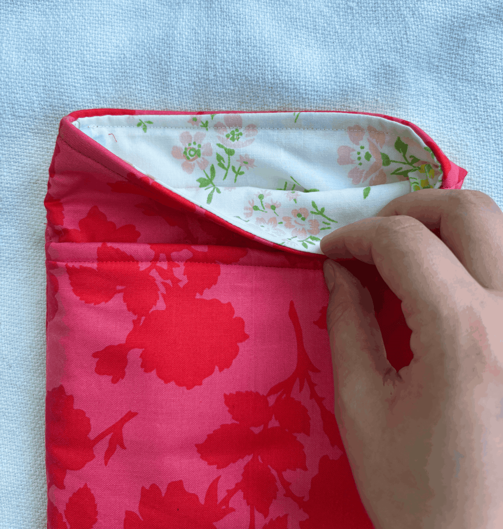 A close-up of a book sleeve with a bright pink floral exterior and a white floral lining, being held open by a person's hand against a light blue textured background.