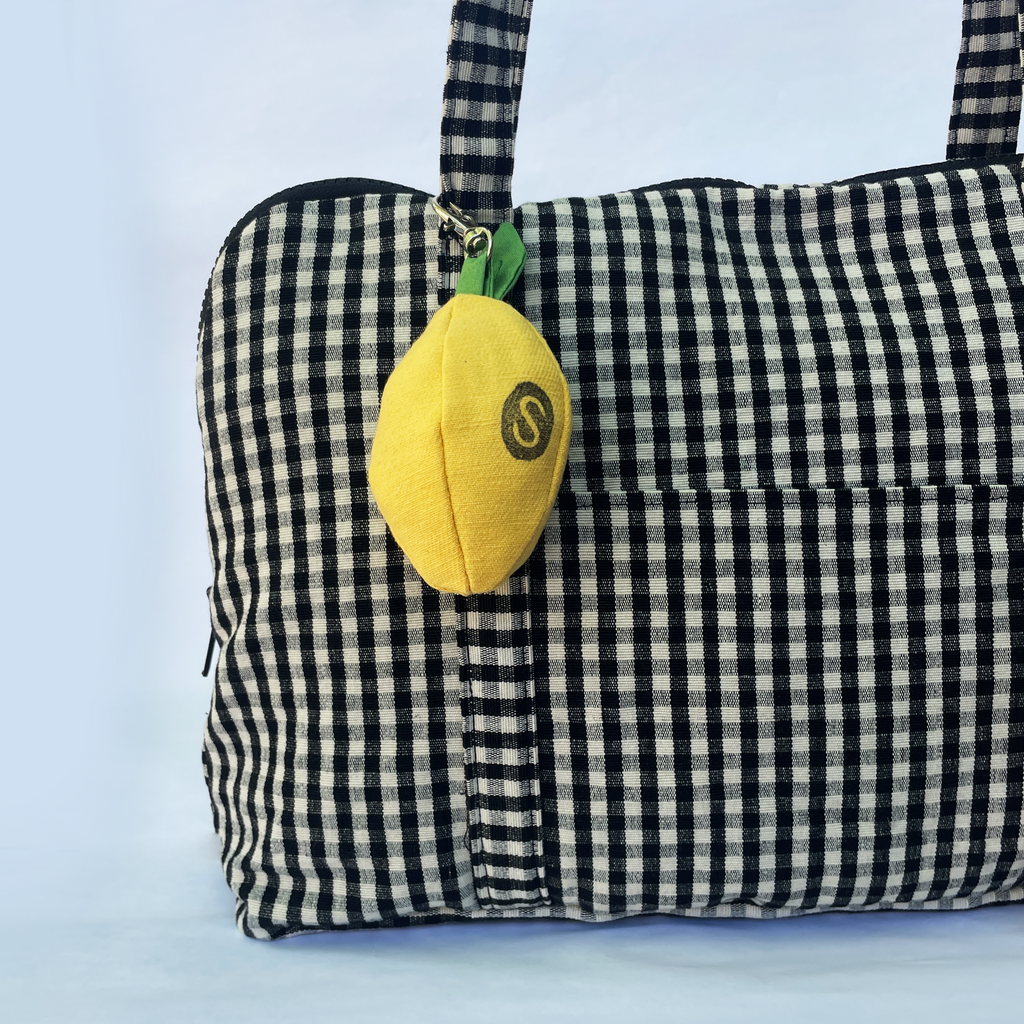 Black and white checkered bag with a yellow lemon-shaped charm on a white background