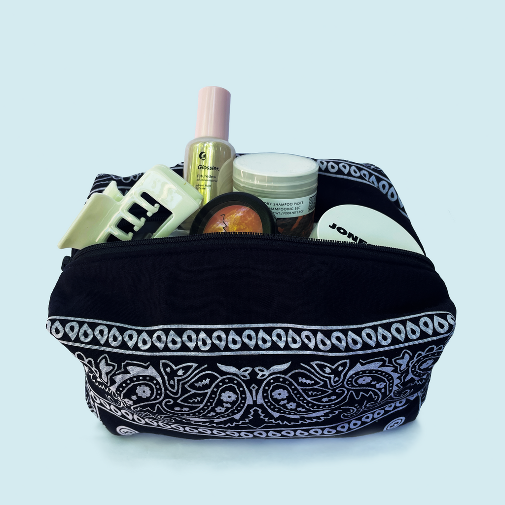 Navy makeup bag with white patterns (bandana print) filled with cosmetic items on a white background