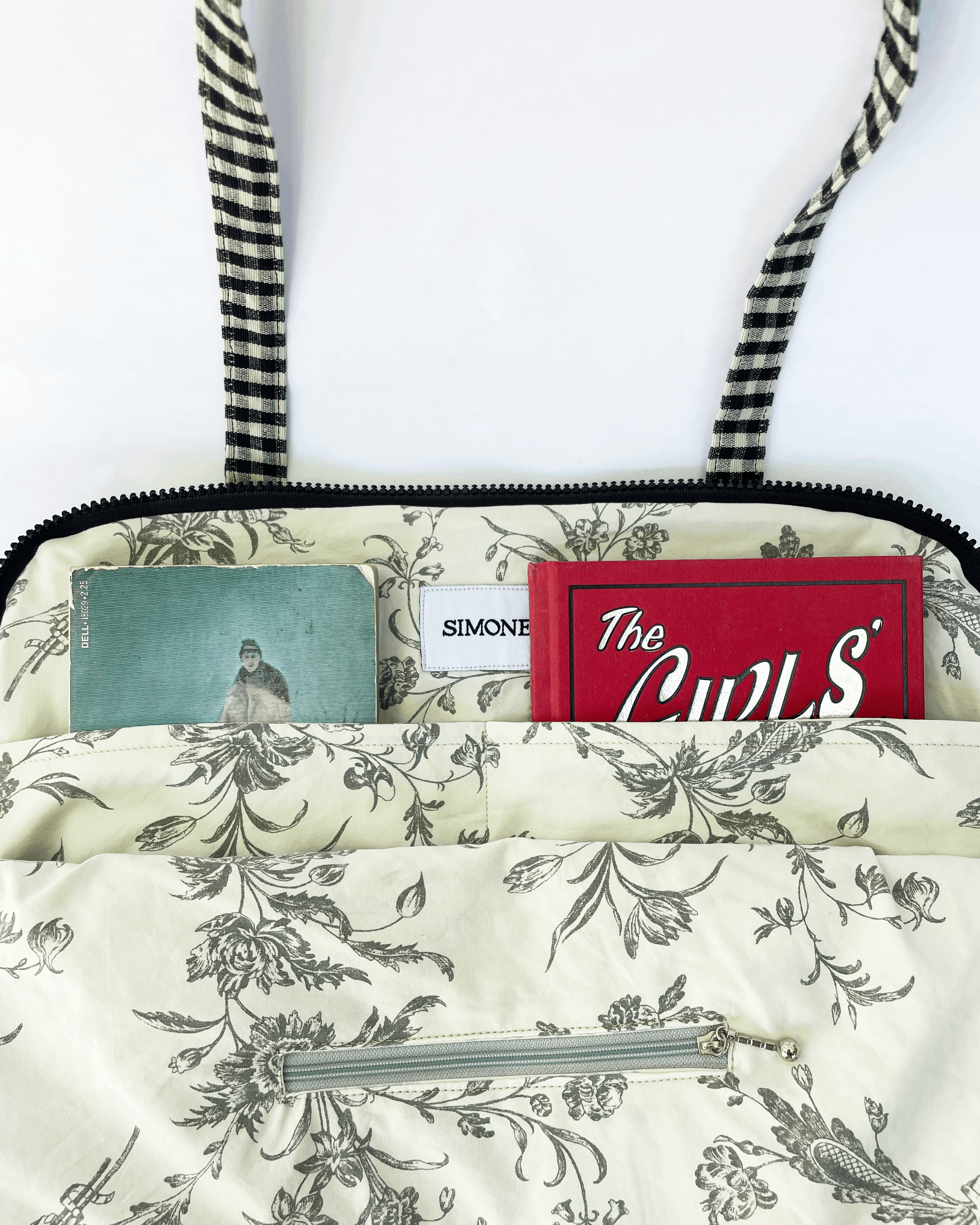Floral-patterned bag lining with a Simone tag on a white background. The lining has two pouches with books in them and one zippered pocket.