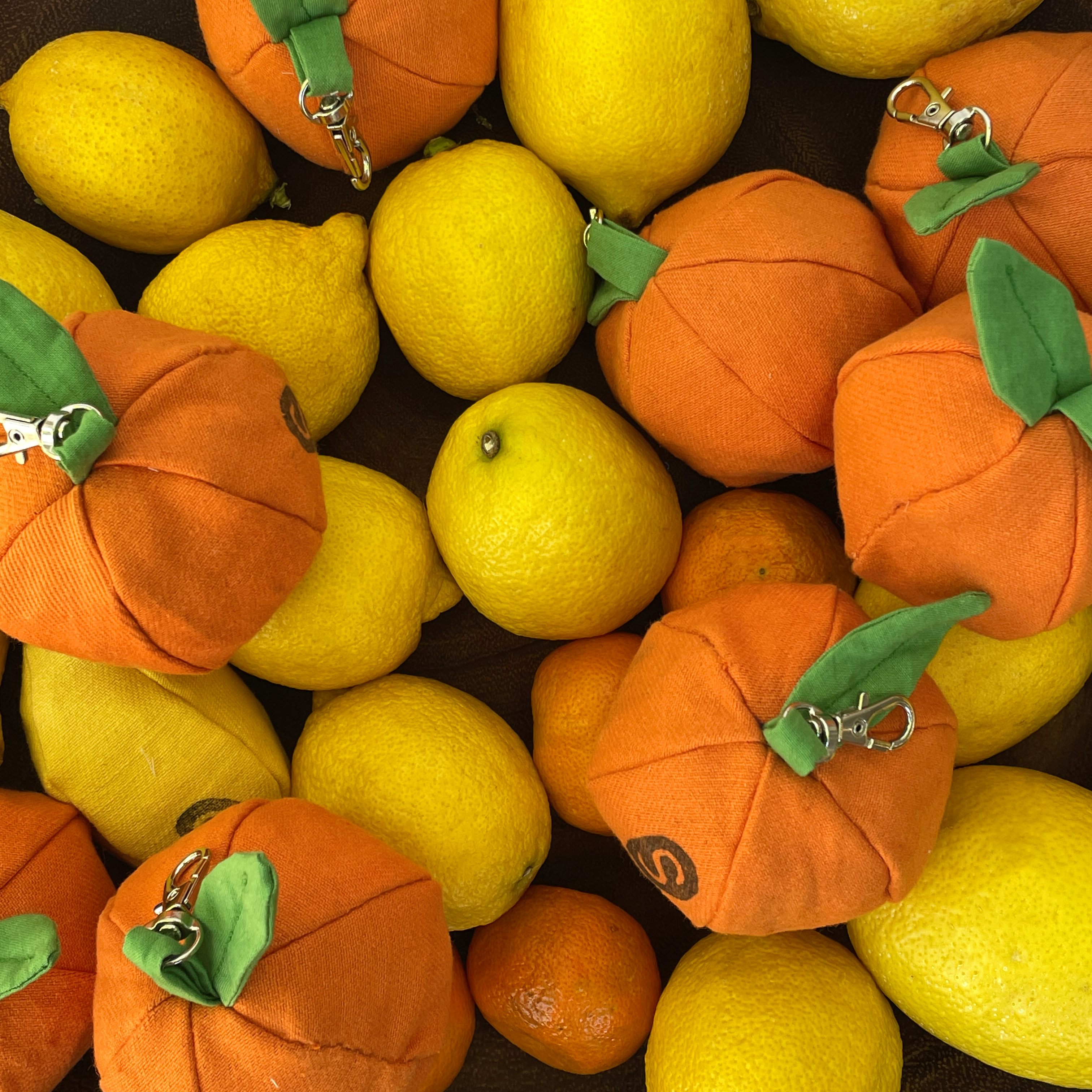 Orange and lemon plush keychains with green stems on a bed of lemons.